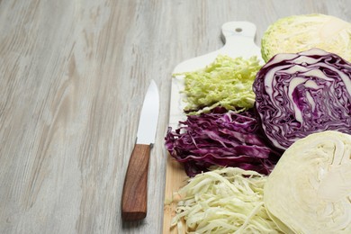 Photo of Different types of cut cabbage and knife on white wooden table, space for text
