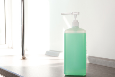 Photo of Dispenser bottle with green antiseptic gel on wooden shelf indoors. Space for text