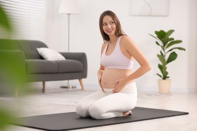 Photo of Pregnant woman sitting on yoga mat at home