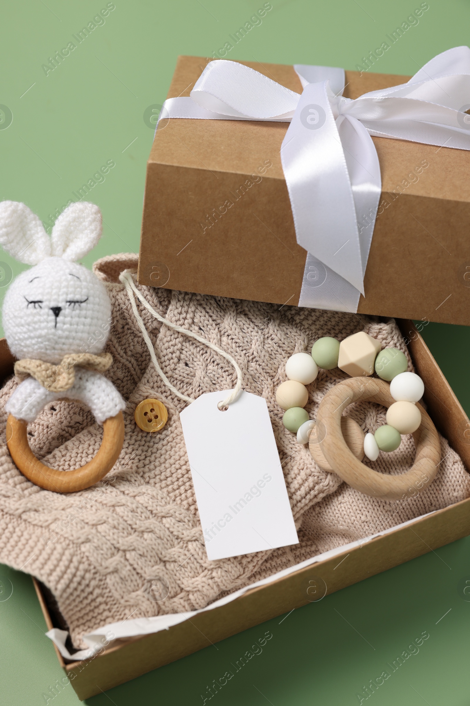 Photo of Different baby accessories, knitted sweater and blank card in box on green background