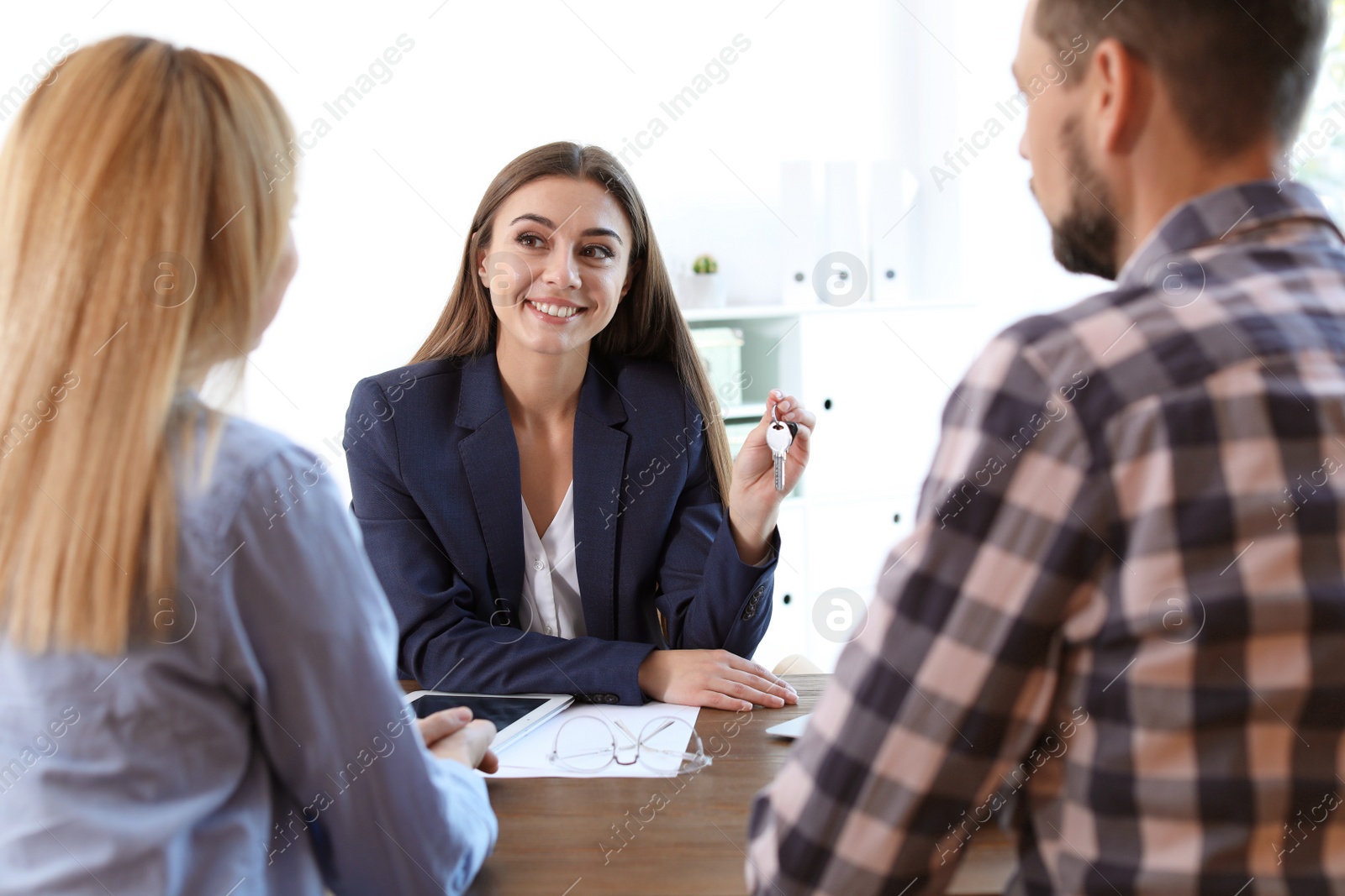 Photo of Female real estate agent showing house key to couple at table in office