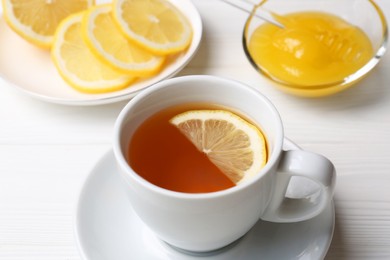 Photo of Cup with delicious immunity boosting tea, lemon and honey on white wooden table, closeup
