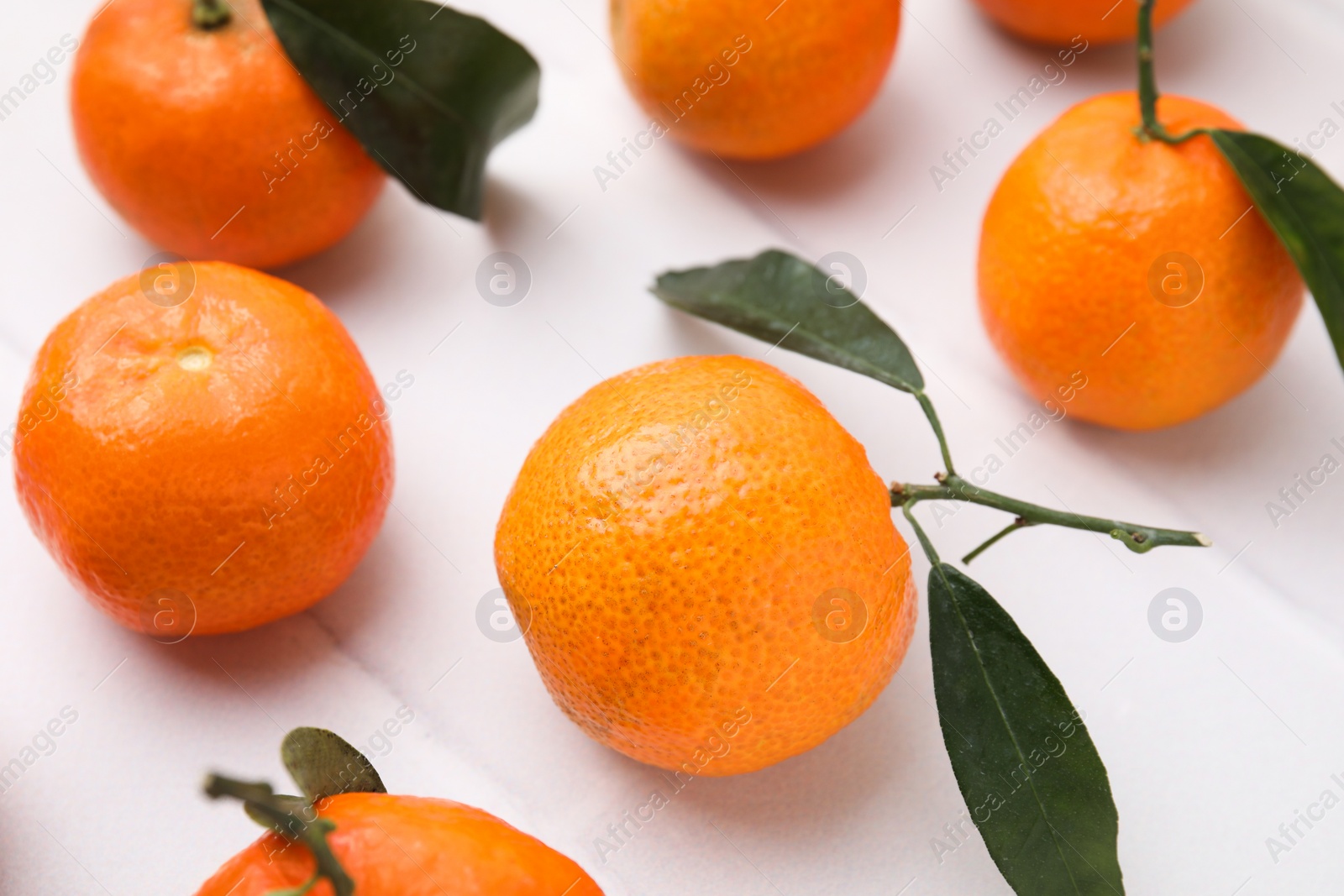 Photo of Fresh ripe tangerines with green leaves on white table, closeup