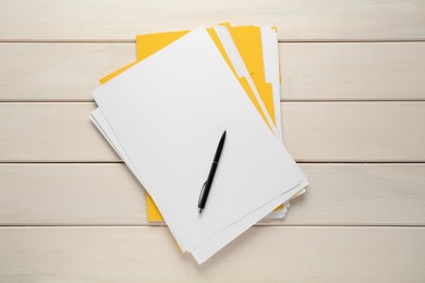 Yellow files with blank sheets of paper and pen on white wooden table, top view. Space for design