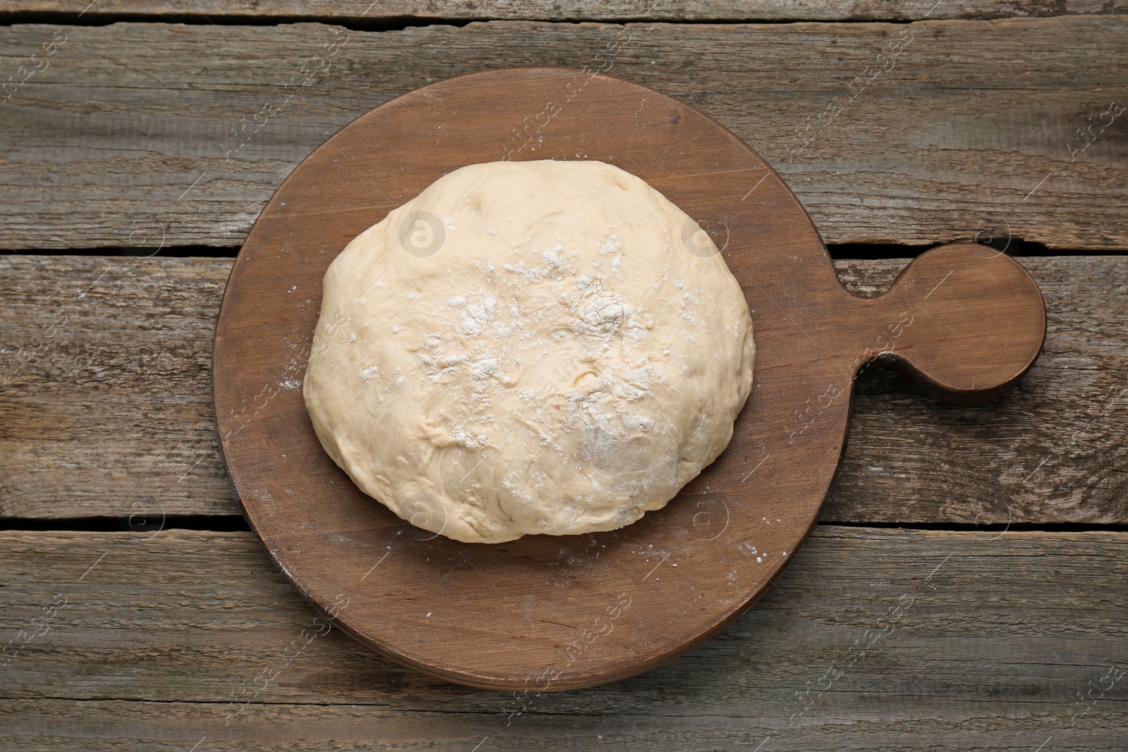Photo of Fresh yeast dough with flour on wooden table, top view