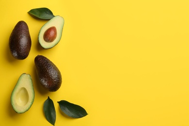 Whole and cut ripe avocadoes with green leaves on yellow background, flat lay. Space for text