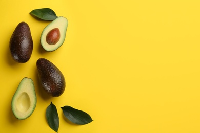 Photo of Whole and cut ripe avocadoes with green leaves on yellow background, flat lay. Space for text