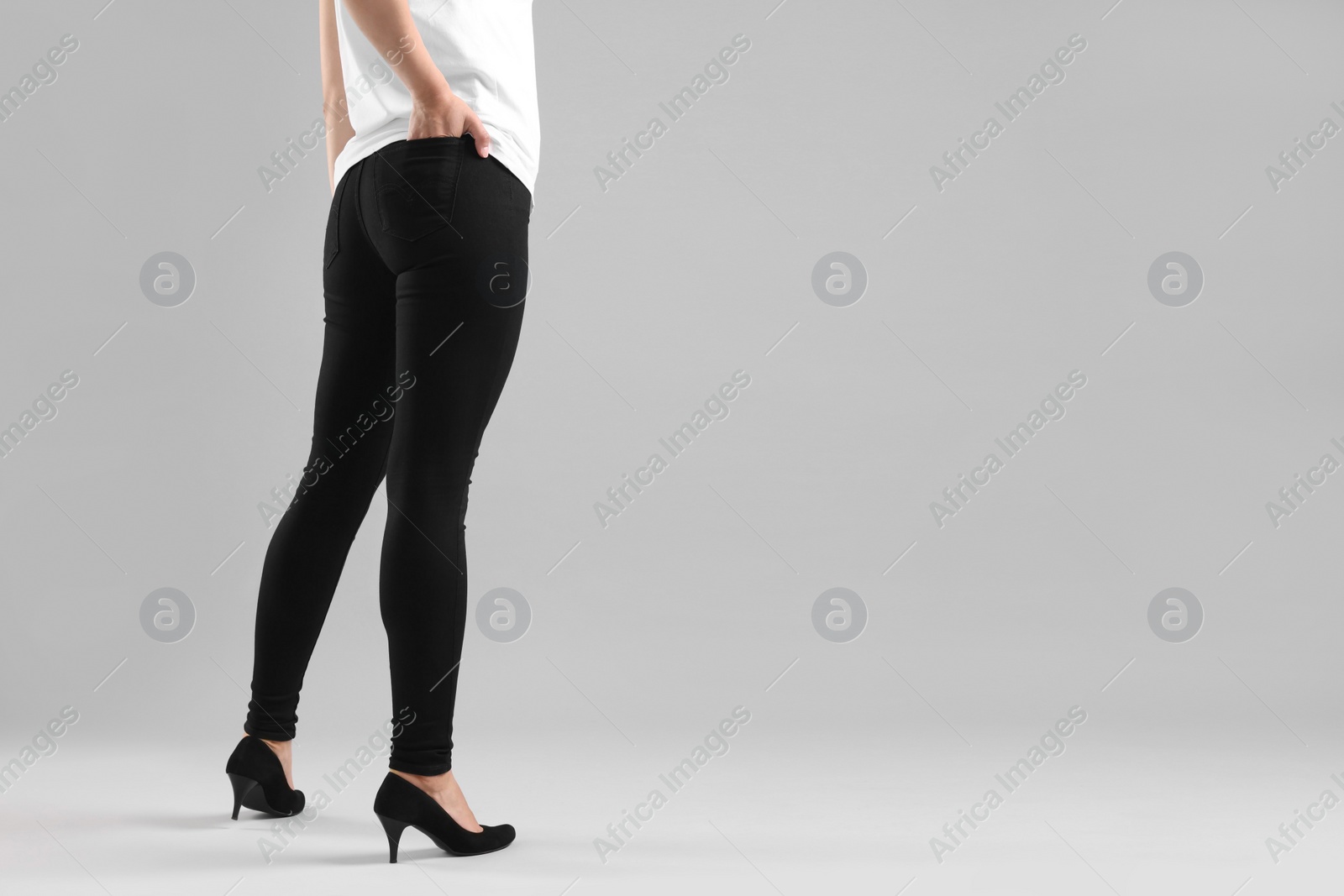 Photo of Woman wearing stylish black jeans and high heels shoes on light gray background, closeup. Space for text