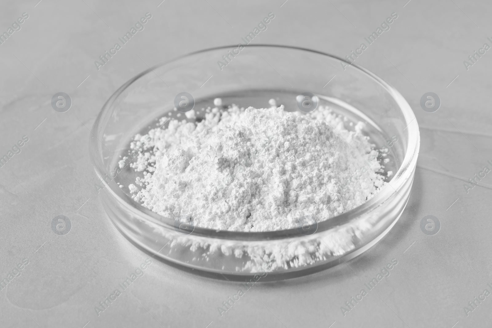 Photo of Petri dish with calcium carbonate powder on grey table, closeup