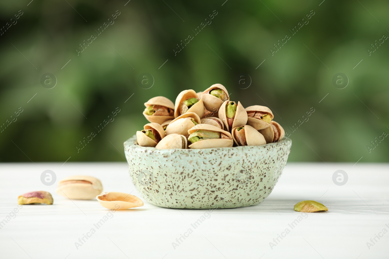 Photo of Tasty pistachios in bowl on white table against blurred background