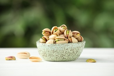 Tasty pistachios in bowl on white table against blurred background