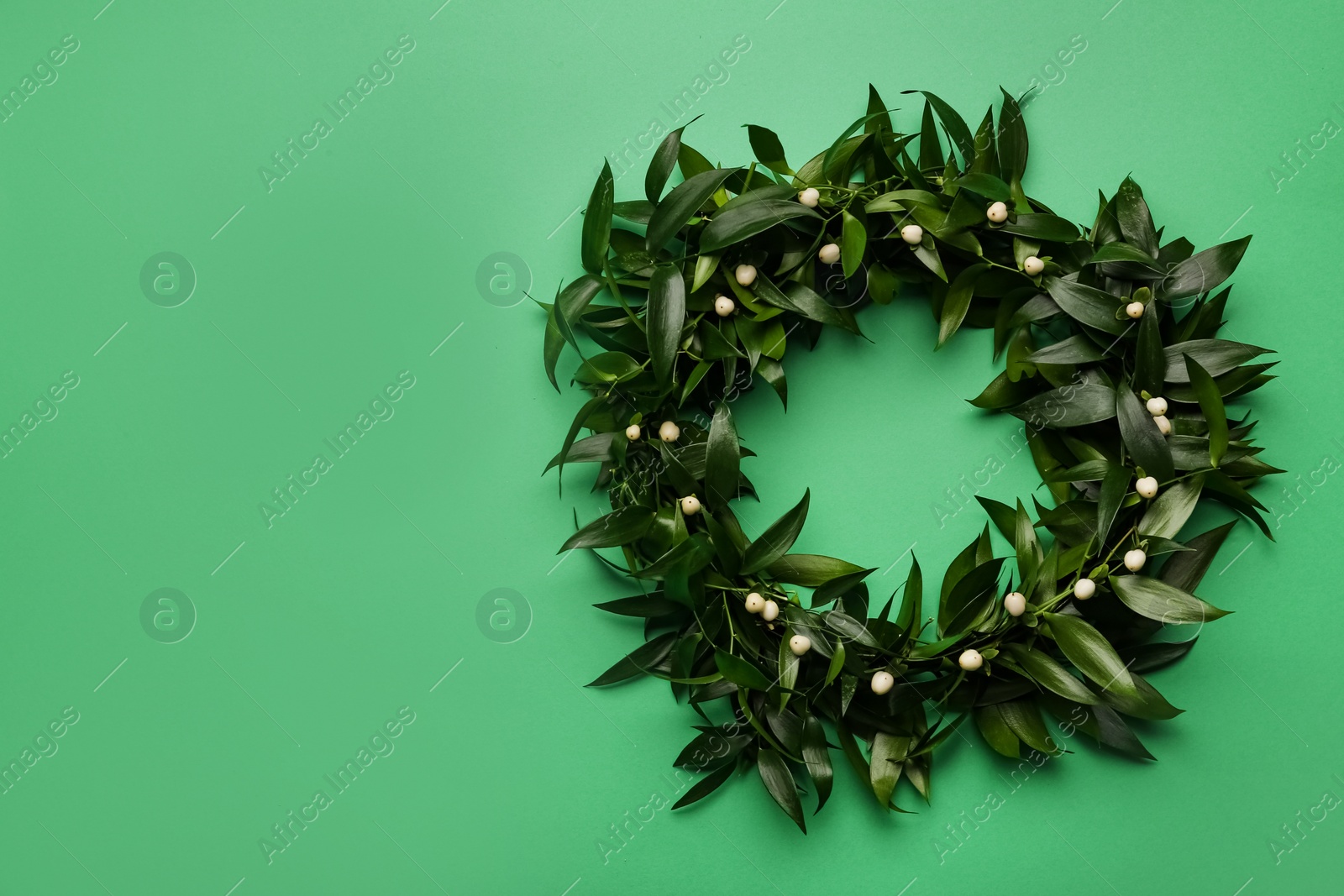 Photo of Beautiful handmade mistletoe wreath on green background, top view. Space for text