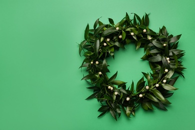 Beautiful handmade mistletoe wreath on green background, top view. Space for text