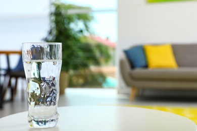 Glass of water on table in room, space for text. Refreshing drink