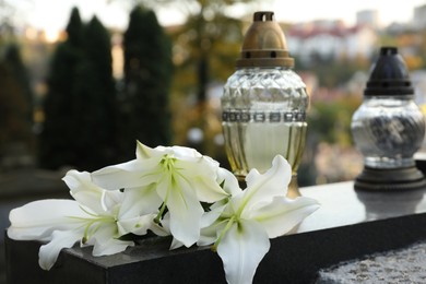 Photo of White lilies and grave lights on granite tombstone outdoors. Funeral ceremony
