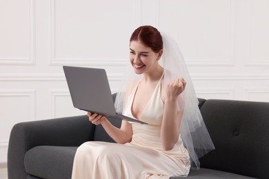 Photo of Cheerful bride with laptop on couch indoors