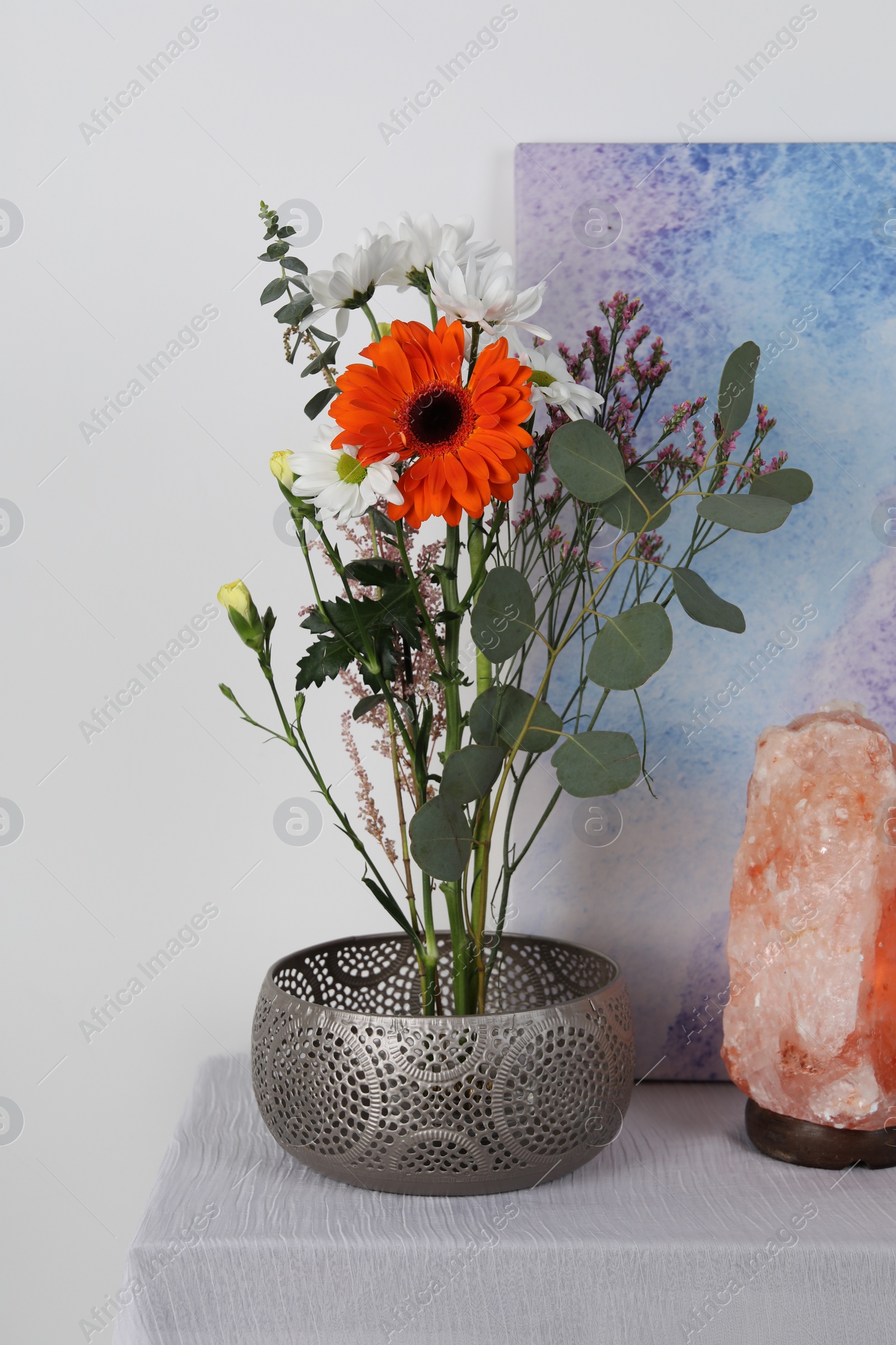 Photo of Stylish ikebana as house decor. Beautiful fresh flowers and eucalyptus branch on table near picture and salt lamp indoors