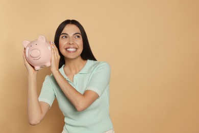Happy young woman with ceramic piggy bank on beige background, space for text