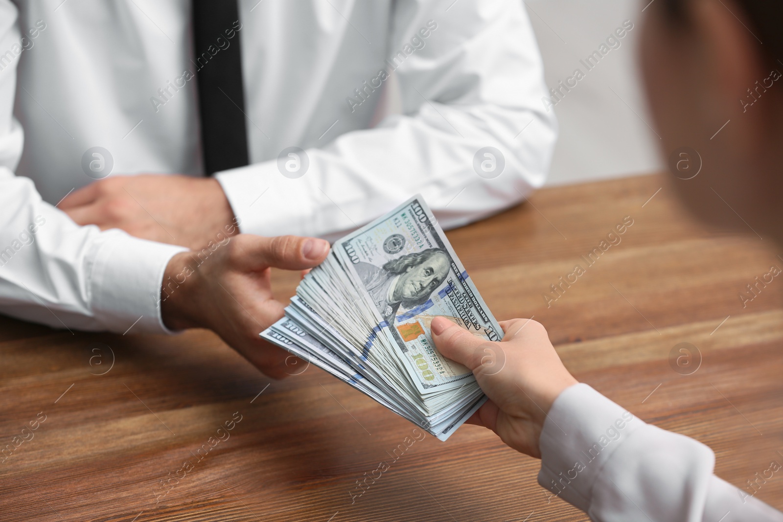 Photo of Woman giving bribe money to man at table indoors, closeup