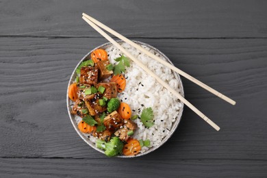 Bowl of rice with fried tofu, broccoli and carrots on grey wooden table, top view