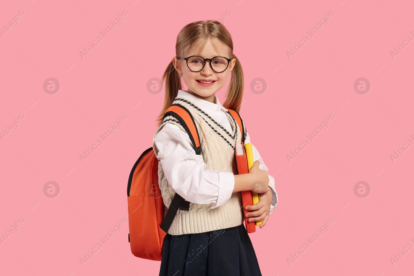 Photo of Happy schoolgirl in glasses with backpack and books on pink background