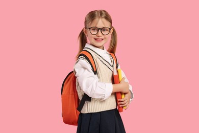 Photo of Happy schoolgirl in glasses with backpack and books on pink background