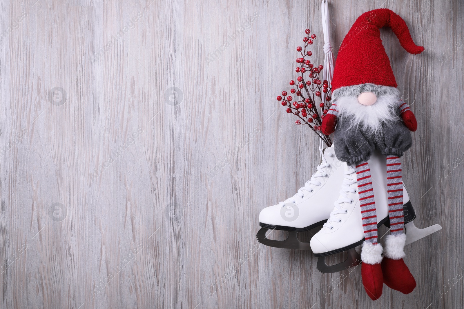 Photo of Pair of ice skates with Christmas gnome and decorative branches hanging on wooden wall, space for text