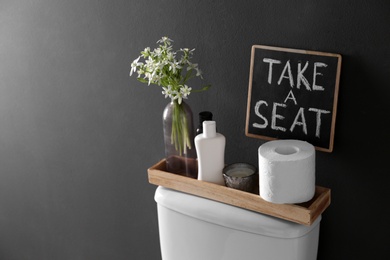 Decor elements, necessities and toilet bowl near black wall, space for text. Bathroom interior