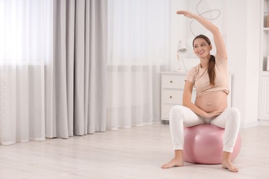 Photo of Pregnant woman doing exercises on fitness ball in room, space for text. Home yoga