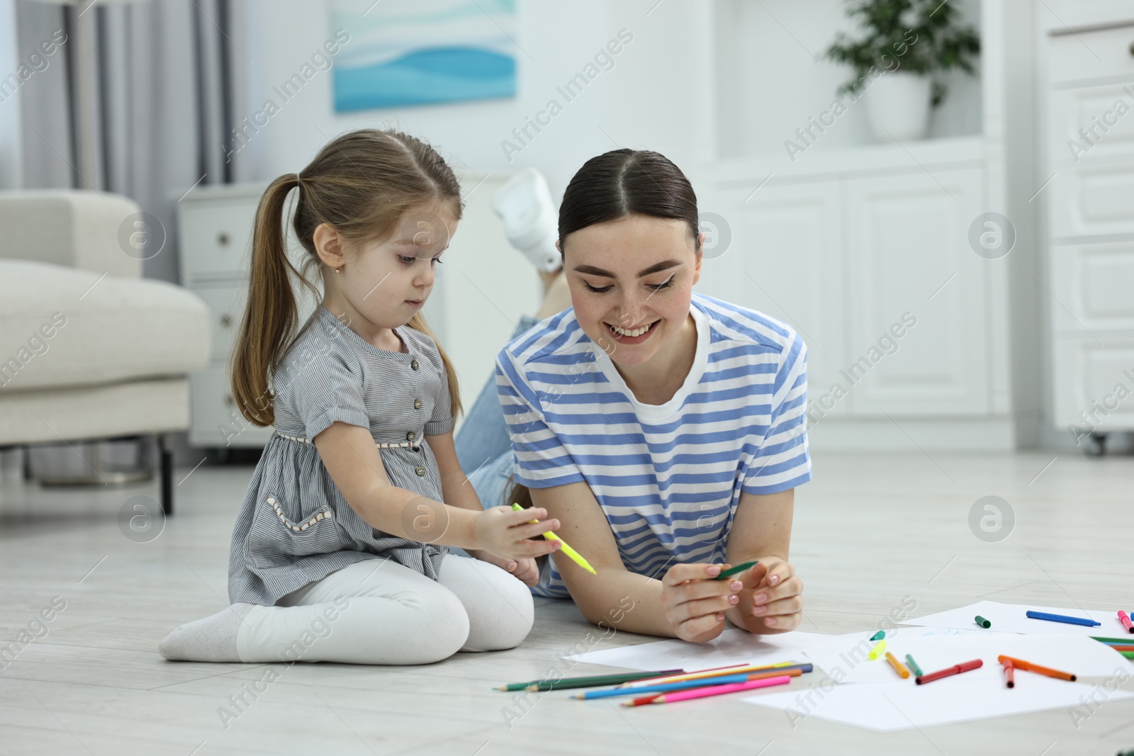 Photo of Mother and her little daughter drawing with colorful markers on floor at home