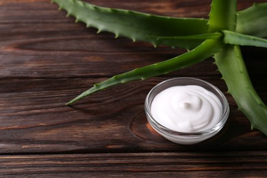 Photo of Bowl of cosmetic cream and aloe vera leaves on wooden table, closeup. Space for text