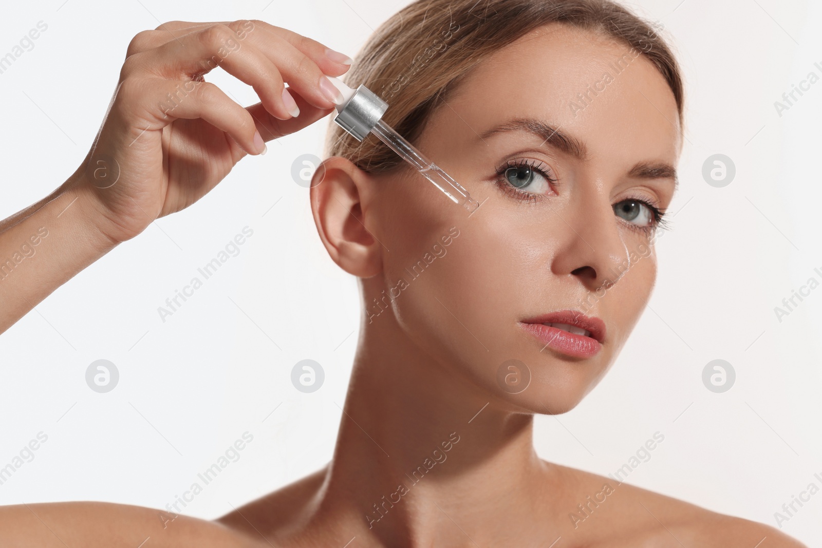 Photo of Beautiful woman applying cosmetic serum onto her face on white background, closeup