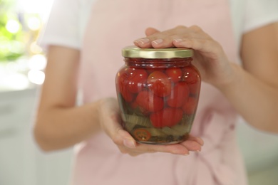 Woman holding jar of pickled tomatoes indoors, closeup