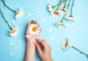 Woman with beautiful chamomile flowers on color background, top view