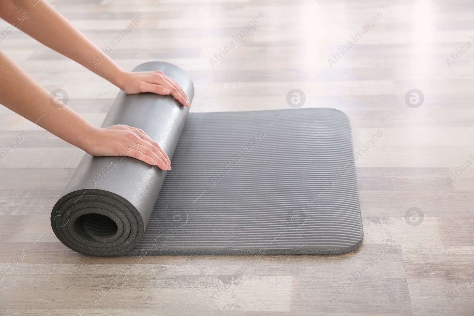 Photo of Woman rolling yoga mat on floor indoors, closeup