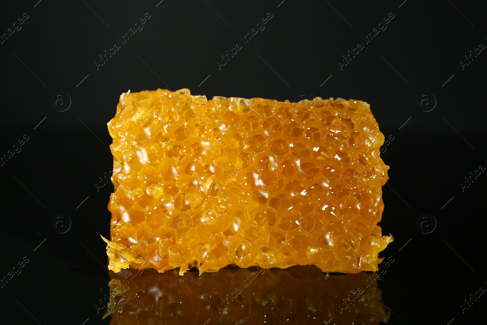 Photo of Piece of natural honeycomb with tasty honey on black background