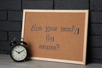 Cork board with phrase Are You Ready For Exams? on wooden table near black brick wall