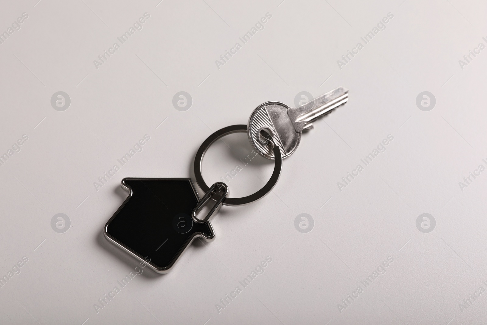 Photo of Key with trinket in shape of house on white background, top view. Real estate agent services