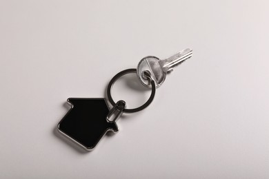 Key with trinket in shape of house on white background, top view. Real estate agent services