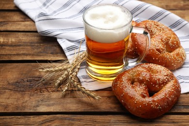 Tasty pretzels, glass of beer and wheat spikes on wooden table