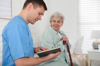 Caregiver reading book to senior woman indoors. Home health care service