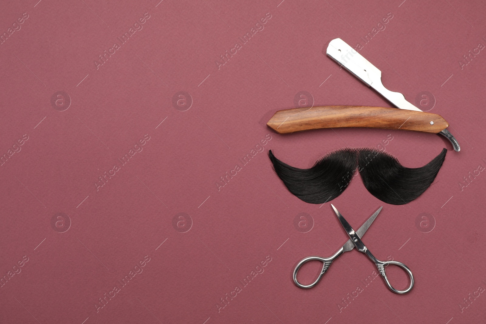 Photo of Artificial moustache and barber tools on burgundy background, flat lay. Space for text