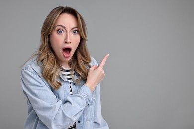 Portrait of surprised woman pointing at something on grey background. Space for text