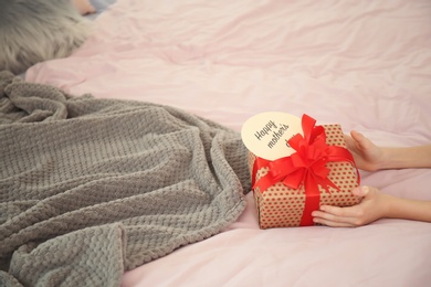 Photo of Little child putting gift box for Mother's Day on bed