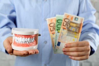 Photo of Woman holding educational dental typodont model and euro banknotes on light background, closeup. Expensive treatment