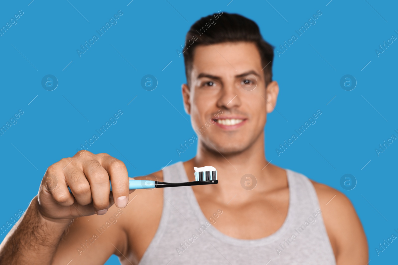 Photo of Man holding toothbrush with paste against blue background, focus on hand