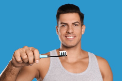 Man holding toothbrush with paste against blue background, focus on hand