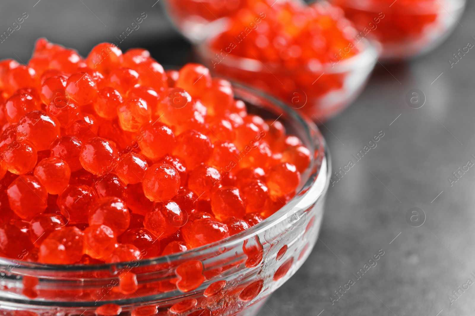 Photo of Glass bowl with delicious red caviar on table, closeup