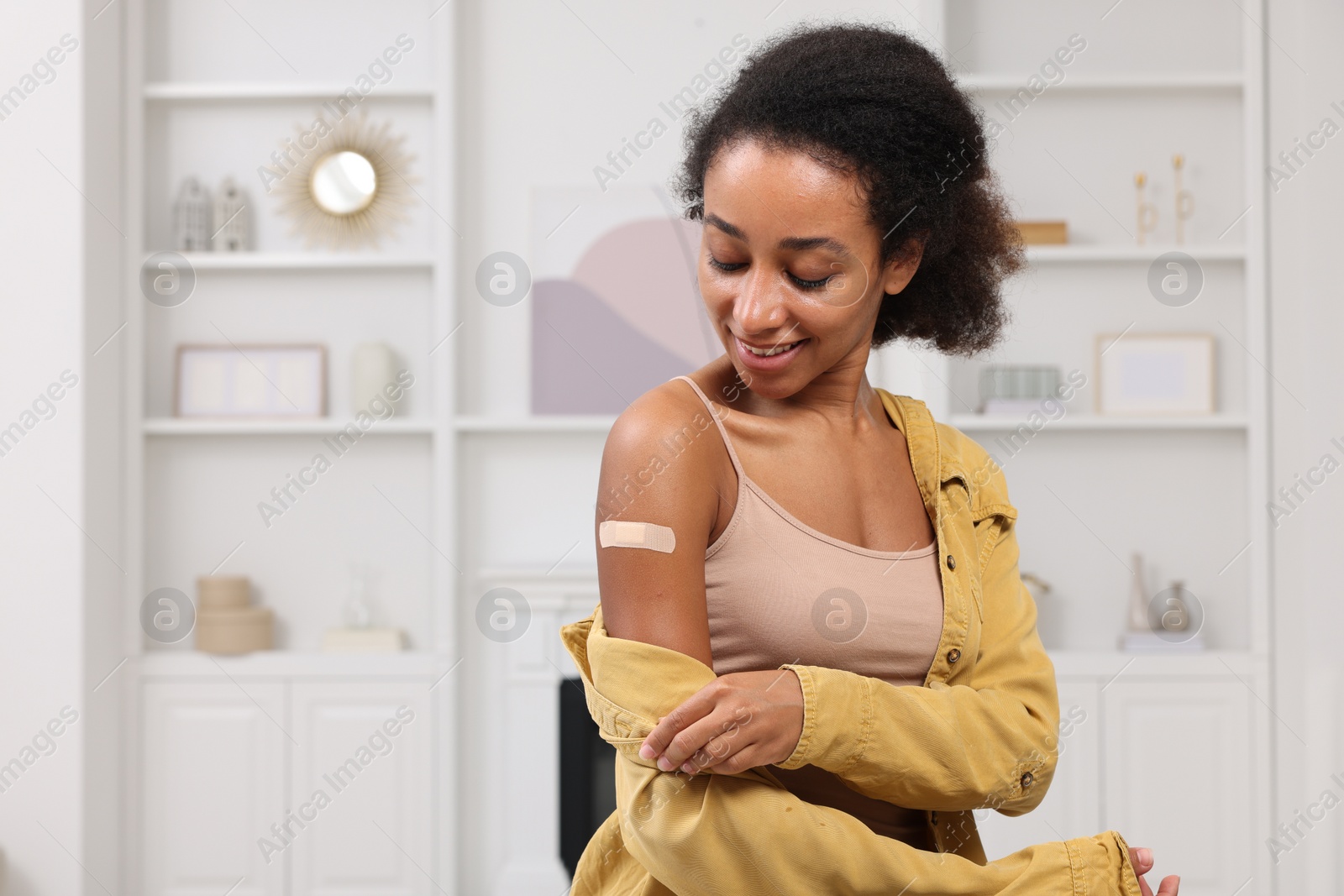 Photo of Happy young woman with adhesive bandage on her arm after vaccination indoors. Space for text