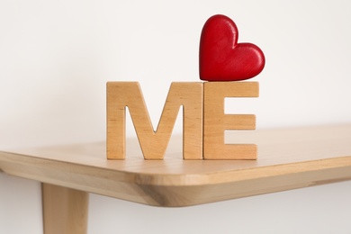 Photo of Phrase Love Me made of red heart and wooden letters on shelf, closeup